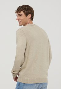 Beżowy sweter dziany z okrągłym dekoltem, ściągaczami przy mankietach i u dołu. Tkanina ma teksturowane wykończenie, zaprezentowane z lekko obróconej pozycji.