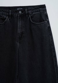 Jeans de mezclilla negra con un diseño clásico, que cuentan con cierre de botón, bolsillos frontales y una textura suave. Detalle de costura visible.