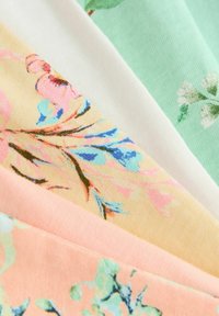 Gros plan de tissus pastel pliés avec des imprimés floraux délicats dans des tons rose, bleu, vert et blanc disposés en éventail superposé.