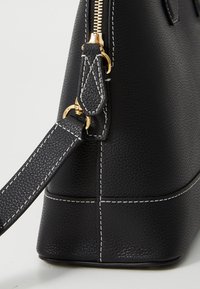 Borsa a mano in pelle nera con finitura testurizzata, accessori in oro e cuciture bianche. Il design include una chiusura con zip e una tracolla staccabile.