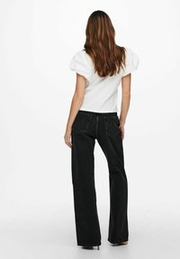 Top blanco de manga abullonada combinado con jeans de pierna ancha negros de cintura alta. Los jeans cuentan con dos bolsillos traseros y una textura suave.