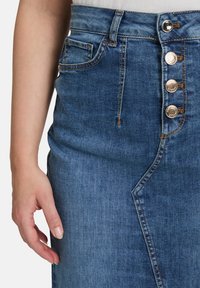 Jupe en denim bleu foncé avec un design droit. Dotée d'une taille à cinq boutons, de poches latérales et de coutures contrastées. Texture lisse.