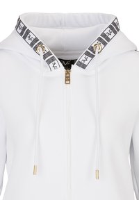 Bílá mikina na zip s černým vzorovaným límcem, zlatými kovovými doplňky a šňůrkami. Měkká látka s moderním, přiléhavým střihem.