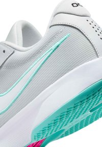 Chaussure de sport blanche avec tige en mesh, accents turquoise et détails roses sur la semelle. Surface texturée et motif de couture distinctif.