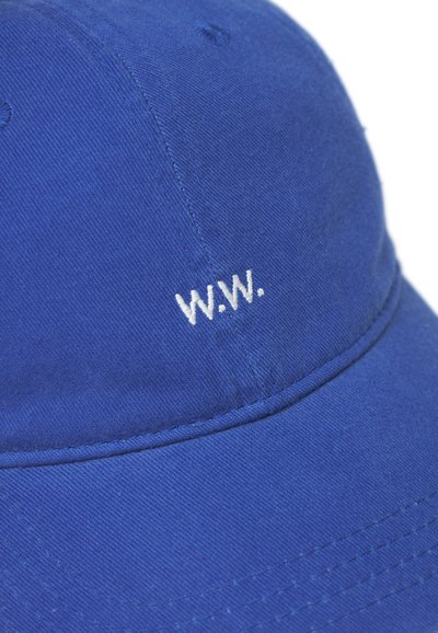 Sinine puuvillane müts, mille ees on tikitud valge "W.W." logo, kumerate servadega ja jäiga kujuga.