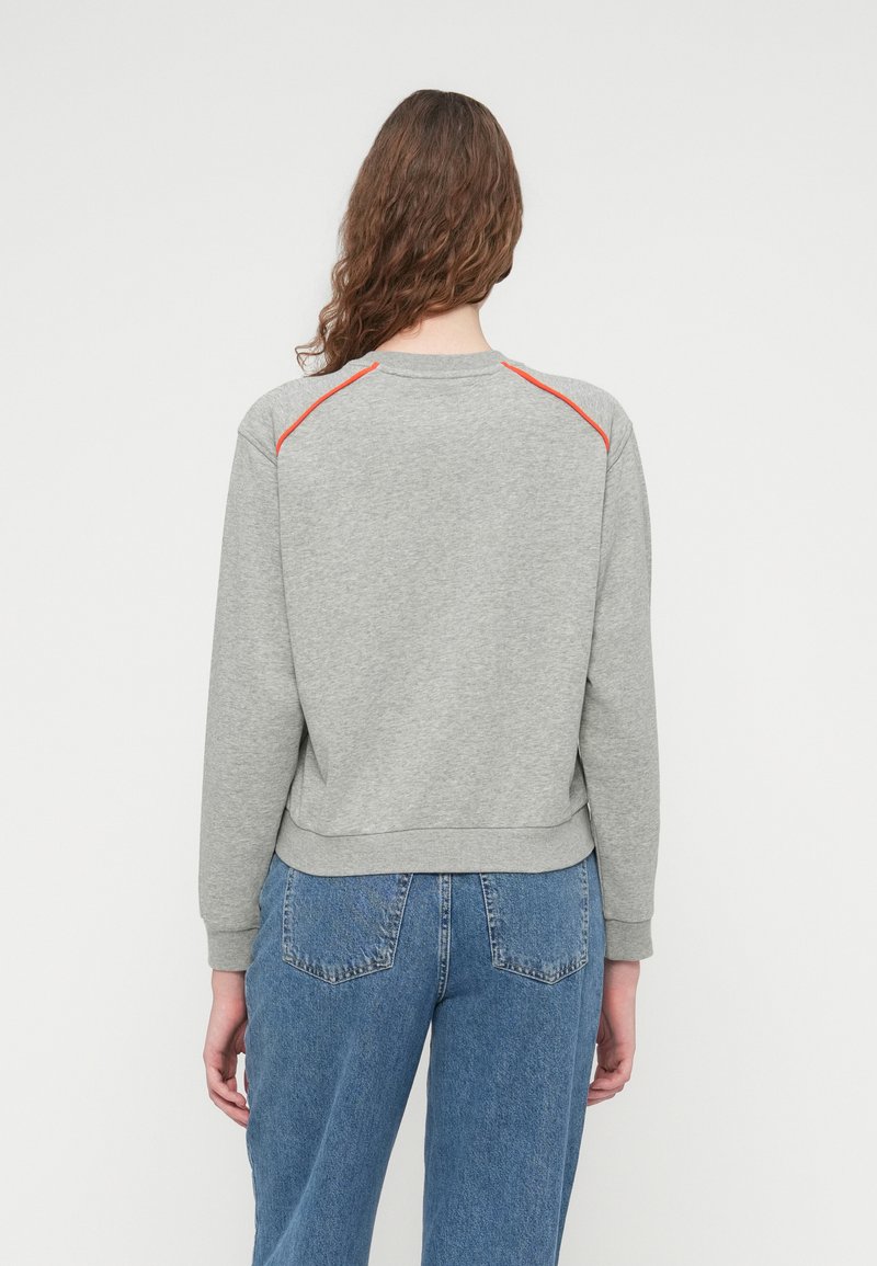 Grå sweatshirt med rund halsudskæring, ribbede manchetter og kant, med røde detaljer på skuldersømmene. Kombineret med blå denimjeans.