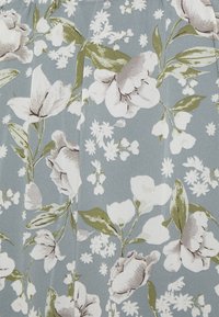 Kukallinen kangas esittelee suuria valkoisia ja harmaita kukkia vihreiden lehtien kera pehmeällä sinisellä taustalla, luoden tekstuurista ilmettä.