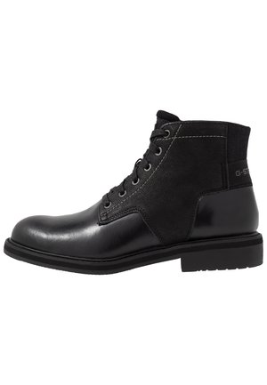 Bottine noire en cuir et tissu avec lacets sur le devant et détail de marque sur le talon, semelle robuste et bout arrondi.