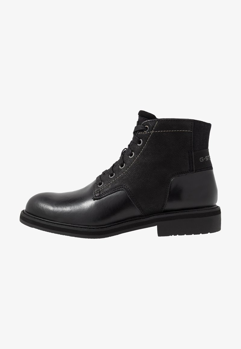 Bottine noire en cuir et tissu avec lacets sur le devant et détail de marque sur le talon, semelle robuste et bout arrondi.