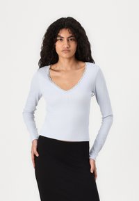 Light blue long-sleeve top with a ribbed texture and a scalloped V-neckline, paired with a black skirt.