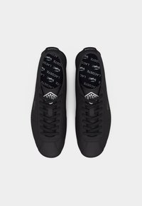 Fekete Lacoste tornacipő pár fűzőkkel, Lacoste logóval a talpbetéteken és az oldalán, felülről fehér háttéren bemutatva.