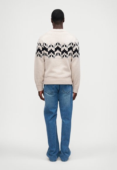 Pulover tricotat bej cu un model geometric în nuanțe de negru și gri pe umeri. Asortat cu blugi de un albastru deschis, cu o croială lejeră și o ușoară decolorare.