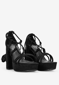 Zapatos de tacón de ante negro con plataforma, tacón grueso, diseño de tiras entrelazadas y punta abierta. Presenta una plantilla acolchada y un detalle de cordones en la parte posterior.