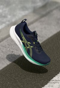 Sportschoen met een marineblauwe bovenkant, groene accenten en een witte tussenzool. Heeft een gestructureerd oppervlak en een opvallend logo, ontworpen voor hardlopen.