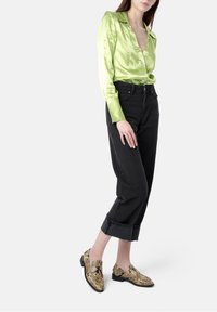 Lime green satin shirt, black high-waisted jeans, and snake-print loafers with a pointed toe and black accents.