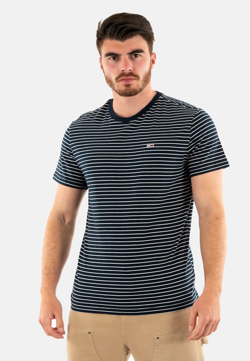 T-shirt à rayures bleu marine et blanches avec un col rond, des manches courtes et un petit emblème sur la poitrine. Tissu en coton léger.