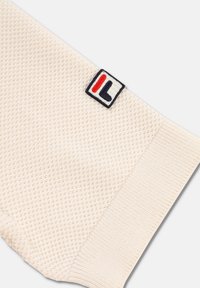 Beżowa, dziana skarpetka z textured pattern, z kontrastową naszywką logo w kolorach czerwonym, białym i niebieskim w okolicy kostki.