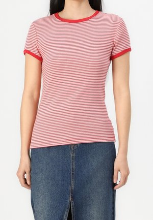 Woman wearing a fitted red and white striped short-sleeve shirt with red trim paired with a blue denim skirt with a front slit.