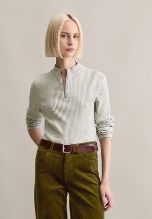 Lichtgrijze geribbelde trui met een halve rits kraag, gecombineerd met olijfgroene corduroy broek en een bruine leren riem met een zilveren gesp.