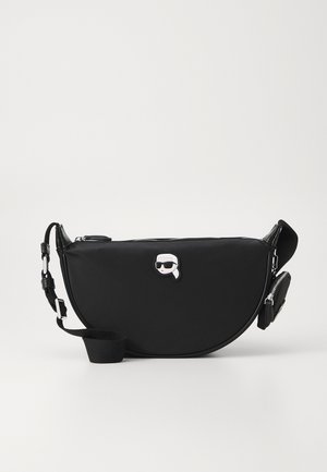 Czarna torebka crossbody w kształcie półksiężyca z regulowanym paskiem, małą zamykaną kieszonką oraz stylizowanym logo twarzy w okularach przeciwsłonecznych na przodzie.