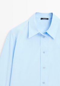 Lichtblauw overhemd met puntkraag, lange mouwen en knoopsluiting aan de voorkant. De stof heeft een gladde textuur met een zachte afwerking.