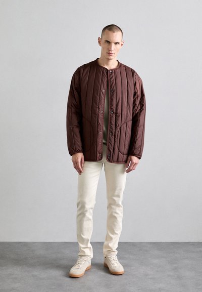 Brown quilted jacket with snap buttons and a round collar, paired with cream-colored jeans and light sneakers. Simple design and relaxed fit.