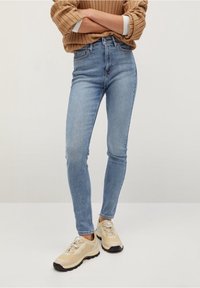 Vaqueros de tiro alto en azul claro, de corte ajustado, con un diseño clásico de cinco bolsillos. Combinados con zapatillas beige que presentan detalles texturizados y cordones.