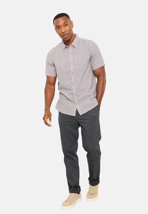 Kurzarmhemd aus hell gemustertem Stoff; mit Knopfleiste; kombiniert mit dunkler Hose und beigen Schuhen.