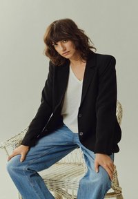 Blazer nero realizzato in un tessuto dalla texture liscia, con due bottoni. Abbina una maglietta bianca a scollo a V e jeans azzurri chiari.