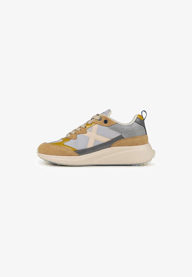 Zapatillas deportivas con una mezcla de materiales de ante y malla en tonos gris, beige y amarillo, con una suela blanca acolchada y una lengüeta trasera.