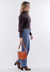 Bruine coltrui, blauwe uitlopende jeans en bruine haklaarsjes. Oranje leren handtas met een korte schouderband en zilveren hardware.