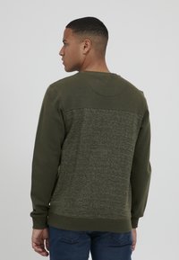 Olijfgroen sweatshirt met een textuurdesign op de achterkant, met horizontale lijnen en een ronde hals. Zacht materiaal, geribde boorden.