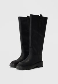 Knee-high black leather boots with a flat sole, rounded toe, vertical seams, and two fabric pull tabs on the shaft for ease of wear.