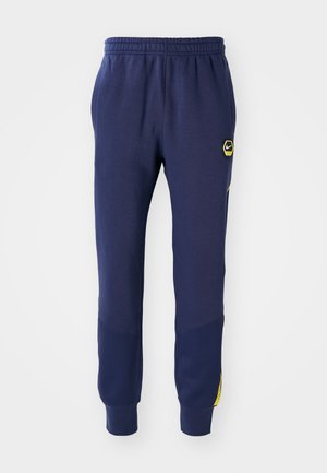 Pantalons de survêtement bleu marine avec taille élastique, poches latérales et patch logo noir/jaune, présentant des accents de panneaux texturés près des chevilles.