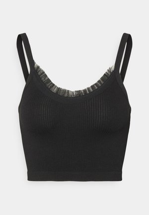 Black ribbed cropped tank top with thin straps and delicate sheer ruffle trim along the neckline against a white background.