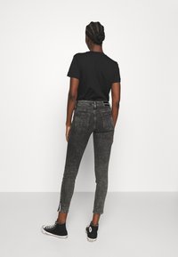 Camiseta negra combinada con jeans ajustados de cintura alta en negro desvaído, con aberturas laterales y clásicas zapatillas altas negras.