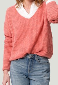 Różowy prążkowany sweter z dekoltem w serek, długimi rękawami i textured knit. Połączony z jasnoniebieskimi dżinsami.