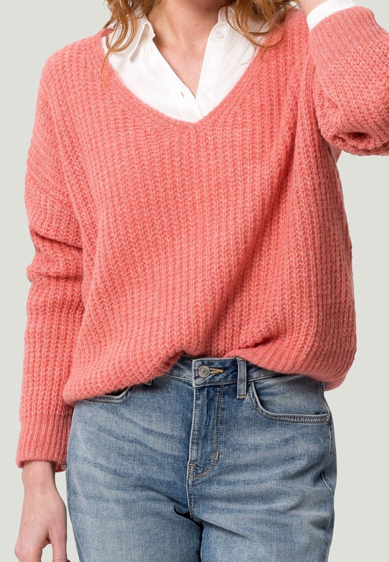 Różowy prążkowany sweter z dekoltem w serek, długimi rękawami i textured knit. Połączony z jasnoniebieskimi dżinsami.
