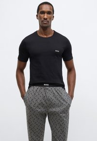 Fekete rövid ujjú póló finom márkajelzéssel és szürke, ismétlődő logókkal mintázott nadrág, mindkettő puha, sima anyagból készült.