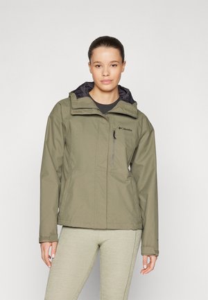 Veste imperméable olive avec une capuche bordée de noir, poche zippée à l'avant et poignets ajustables, portée sur des leggings côtelés gris clair.