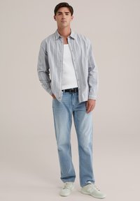 Világoskék csíkos gombos ing, fehér top fölött, világoskék farmernadrággal és világos sportcipővel párosítva. Egyszerű design és laza szabás.
