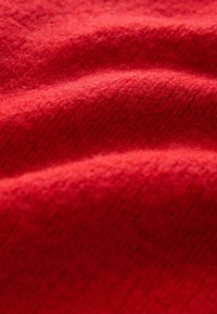 Rødt tekstureret stof med en blød, vævet finish og et let hævet mønster. Materialet virker varmt og indbydende.
