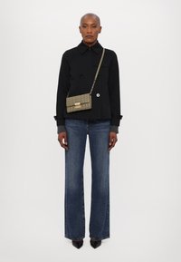 Giacca nera doppiopetto, vestibilità rilassata, abbinata a jeans blu scuri a gamba larga. Gli accessori includono una piccola borsa trapuntata verde oliva.