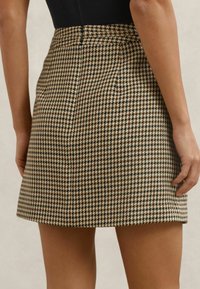 Rudos ir smėlio spalvos letenos rašto sijonas su aptempta liemeniu, trumpu ilgiu ir tekstūruota medžiaga. Turi lygią apdailą ir švarų kraštelį.