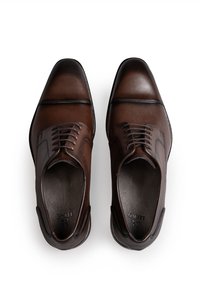 Brązowe skórzane buty wizytowe o gładkim wykończeniu, z zaostrzonym noskiem i wiązane na sznurowadła. Charakteryzują się tonowanym przeszyciem oraz subtelnymi akcentami po bokach.
