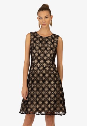 Abito in pizzo nero caratterizzato da un design senza maniche, un motivo floreale e una silhouette fluida. La fodera è di colore nudo, creando un contrasto con il pizzo.