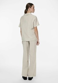 Completo a due pezzi in un tessuto beige chiaro con sottili righe verticali. La parte superiore a maniche corte presenta un colletto, abbinata a pantaloni con gamba larga.