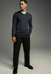 Pulover în nuanță de albastru închis, cu decolteu în V, stil ajustat, asortat cu pantaloni negri și cizme negre. Îmbrăcămintea are linii curate și o textură fină.