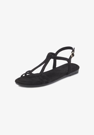 Sandal in suede nero con suola piatta, design a T-strap, fibbia alla caviglia e soletta testurizzata. Aspetto semplice e minimalista.