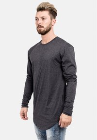 Langärmliges, dunkelgraues T-Shirt aus weichem Stoff mit abgerundetem Saum und Rundhalsausschnitt, kombiniert mit hellblauen, ausgebeulten Jeans.
